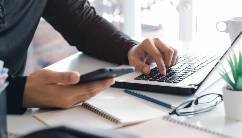 Work using mobile phone typing on computer